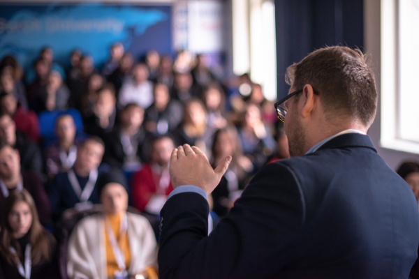 man stands and gestures in front of an audience
