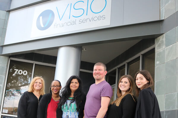6 people stand under a Visio sign