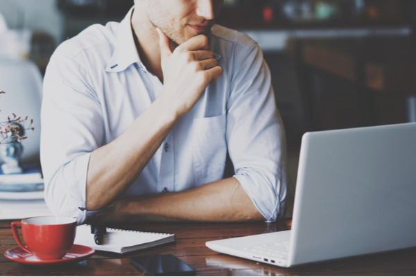 man sitting at table with laptop, notebook, and red cup